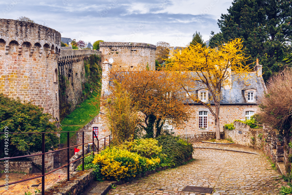 Beautiful view of scenic narrow alley with historic traditional houses and cobbled street in an old town of Dinan with blue sky and clouds. Brittany (Bretagne), France