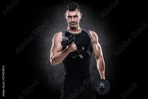 Portrait of sporty healthy cool looking strong muscle charismatic happy smiling handsome man bodybuilder training hard doing heavy weight biceps exercises with dumbbells in black tank top and shorts © Pavel Zenyuk