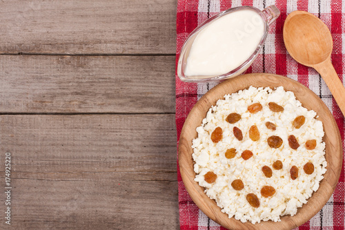 Cottage cheese in bowl with sour cream and raisins on old wooden background with copy space for your text. Top view