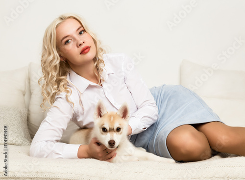 blonde woman with puppy husky dog on a white sofa. girl playing with a dog
