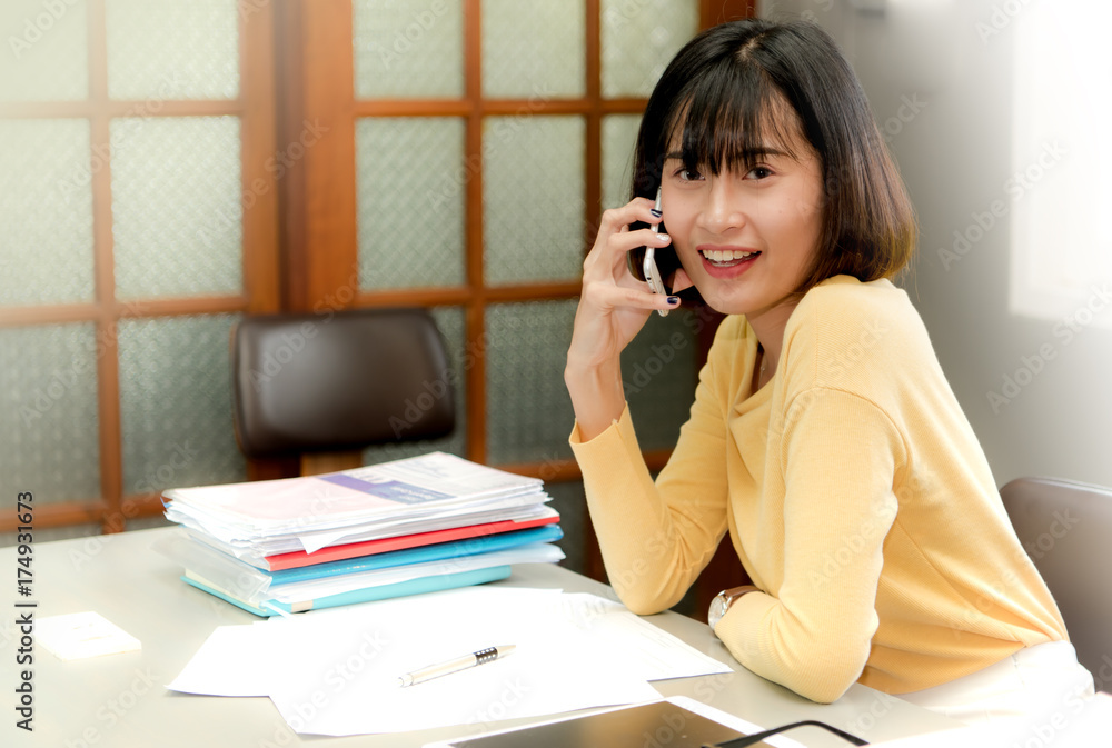 Happy young woman sitting at her desk working and answering a phone call..