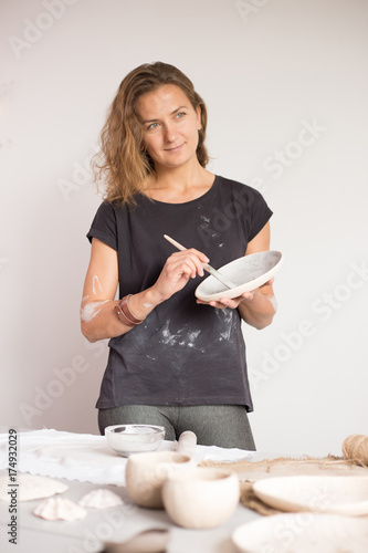 Pretty young woman potter paints a clay cup. Woman working In her pottery studio photo