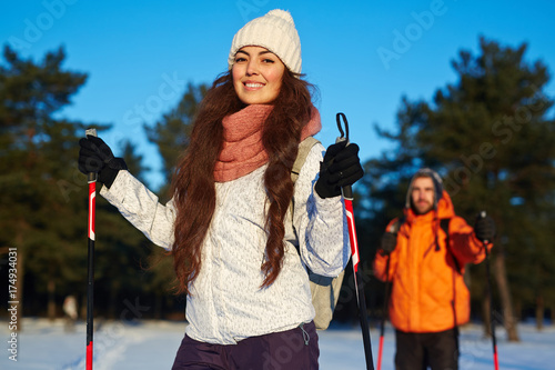 Young woman in activewear skiing with her husband in winter park or forest