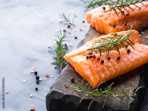 Raw salmon pieces on wooden board with herbs, salt and spices