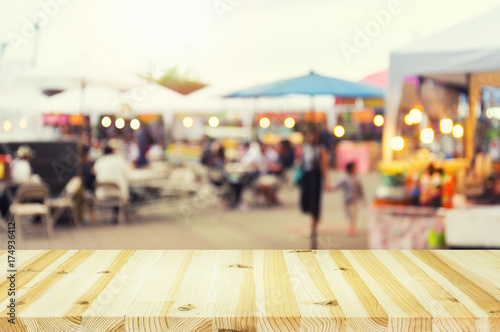 Fotografie Blurred evening food fair in Chiang Mai, Thailand, with market stalls, vendors and visitors, lively street festival atmosphere and wooden table foreground for dining, tourism and event promotion