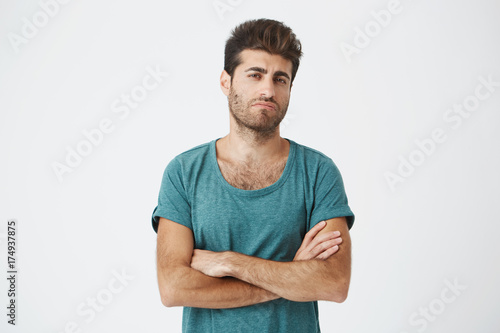 Portrait of confident attractive young spanish guy in blue tshirt and stylish haircut, crossing hands, being super jealous seeing ex girlfriend with new man. photo