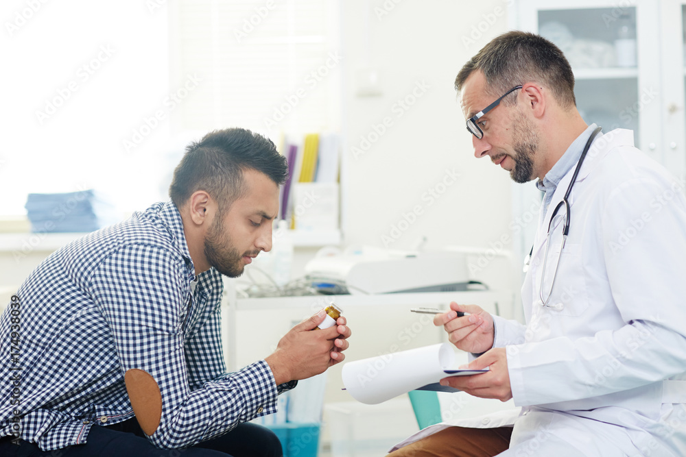 Fototapeta premium Highly professional doctor in eyeglasses consulting male patient about pills while carrying out medical check-up at modern office