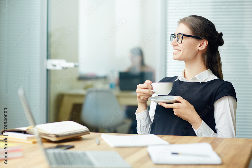 Young female with cup of tea having break by her workplace in office Young female with cup of tea having break by her workplace in office
