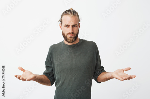 Handsome nordic man with beard and stylish hairdo spreads hands with cynical and mean expression when somebody pushed him on street.