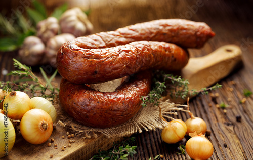 Smoked Polish sausage on a wooden rustic table with addition of fresh aromatic herbs and spices, natural product from organic farm, produced by traditional methods photo