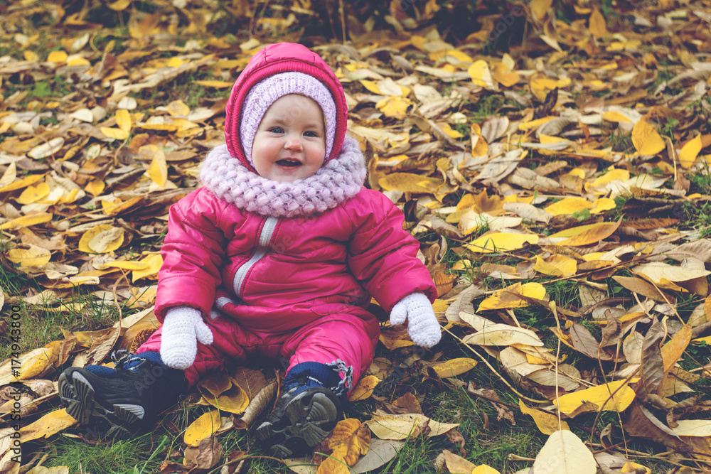 Happy toddler sitting on leaves in autumn park, toned photo Happy toddler sitting on leaves in autumn park, toned photo