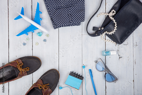 blue bag, sunglasses, shoes, nail polish, earphone note pad and little airplane on white wooden background