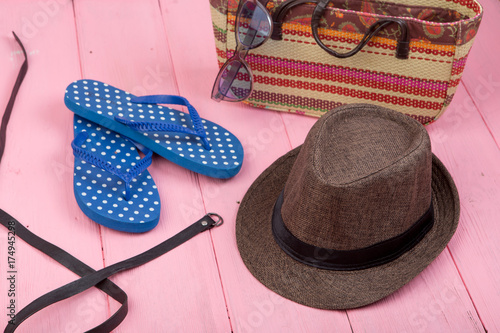 Summer accessories - sunglasses, straw beach bag, sun hat, belt and flip flops on pink wooden table