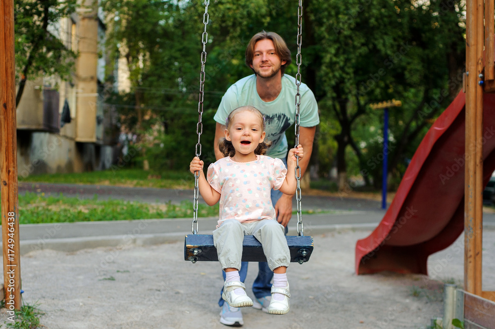 A girl with a dad on the playground on a swing