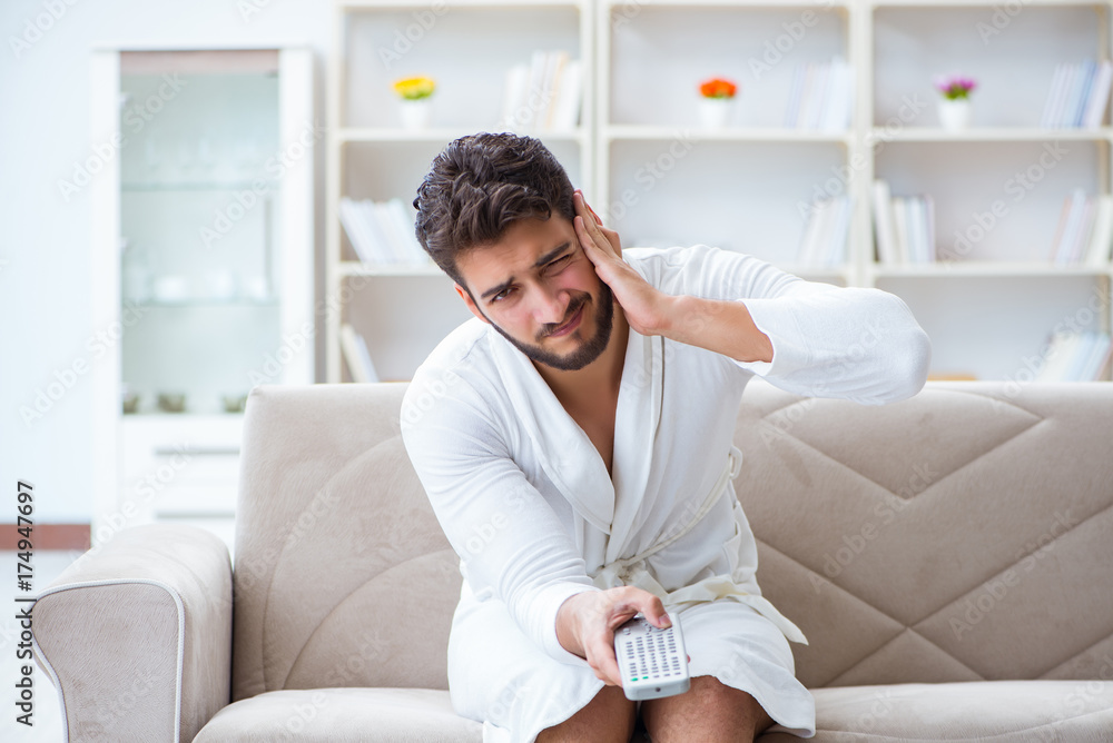 Young man in a bathrobe watching television at home on a sofa co Young man in a bathrobe watching television at home on a sofa co
