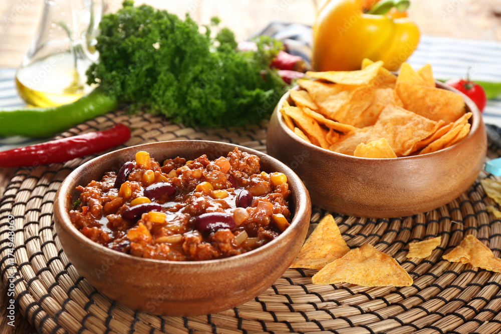 Chili con carne in bowl served with chips on kitchen table