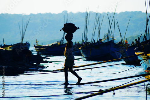 Traditional Indian work. Indian people with a basin full of sand. He unloads the boat that brought a sand from Maharashtra to Goa. Silhouette of the man on the sunset.