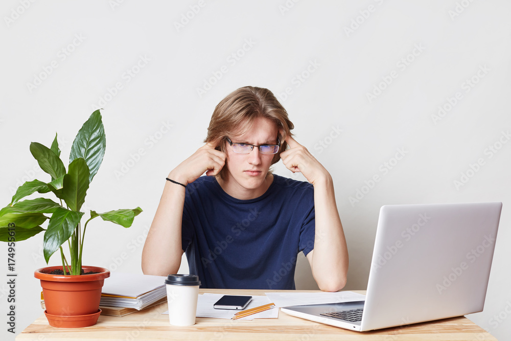 Horizontal portrait of serious male freelancer tries to concentrate, holds hands on temples, works with modern gadgets and documents, isolated over white background. Finding solution in mind
