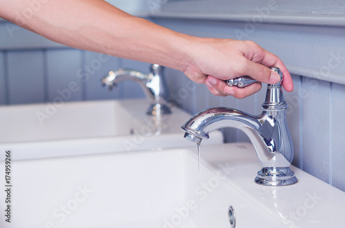 hand man opening silver faucet or water tap with white washing sink in public toilet.