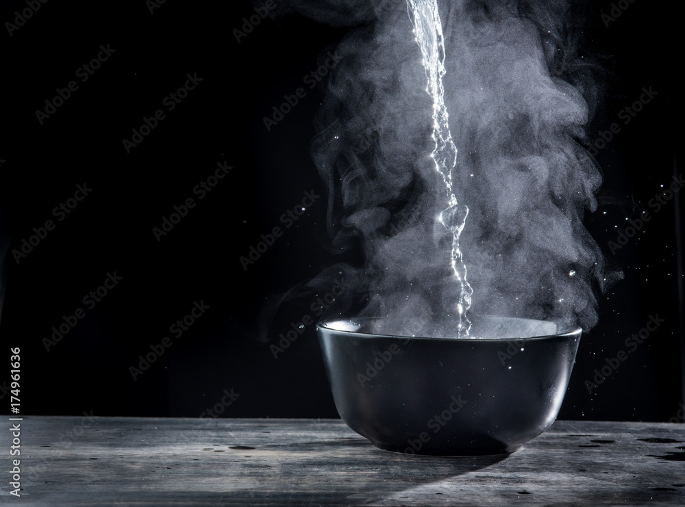 Pouring hot water into into a bowl on a black background