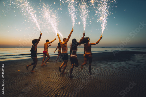 Group of friends having fun running on the beach with sparklers photo