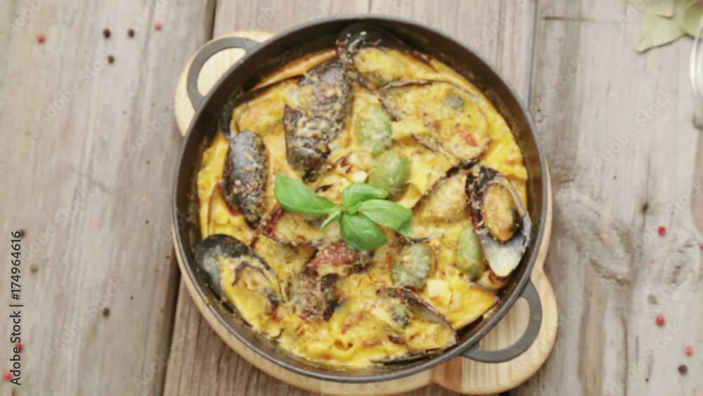 Dish of mussels in cheese sauce on a wooden background with spices. Mussels with cheese baked in a barbecue.
Dish of mussels in cheese sauce on a wooden background with spices. Mussels with cheese baked in a barbecue.