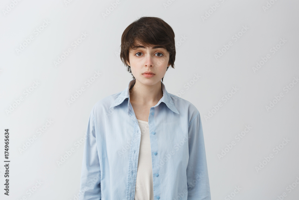 Close up of beautiful young girl with fashionable short haircut and casual clothes looking in camera with unhappy expression. Close up of beautiful young girl with fashionable short haircut and casual clothes looking in camera with unhappy expression.