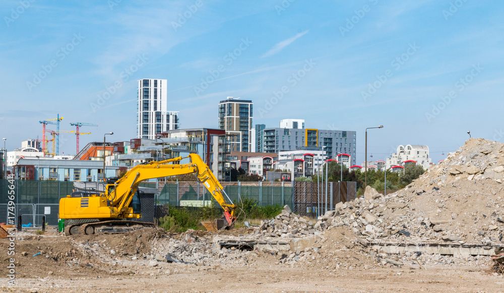 A yellow digger works on the demolition site on Greenwich Millennium Leisure Park. Surrounded by the high rise blocks and concrete rubble pile A yellow digger works on the demolition site on Greenwich Millennium Leisure Park. Surrounded by the high rise blocks and concrete rubble pile
