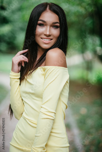young beautiful brunette woman posing in yellow elegance dress at green summer park 