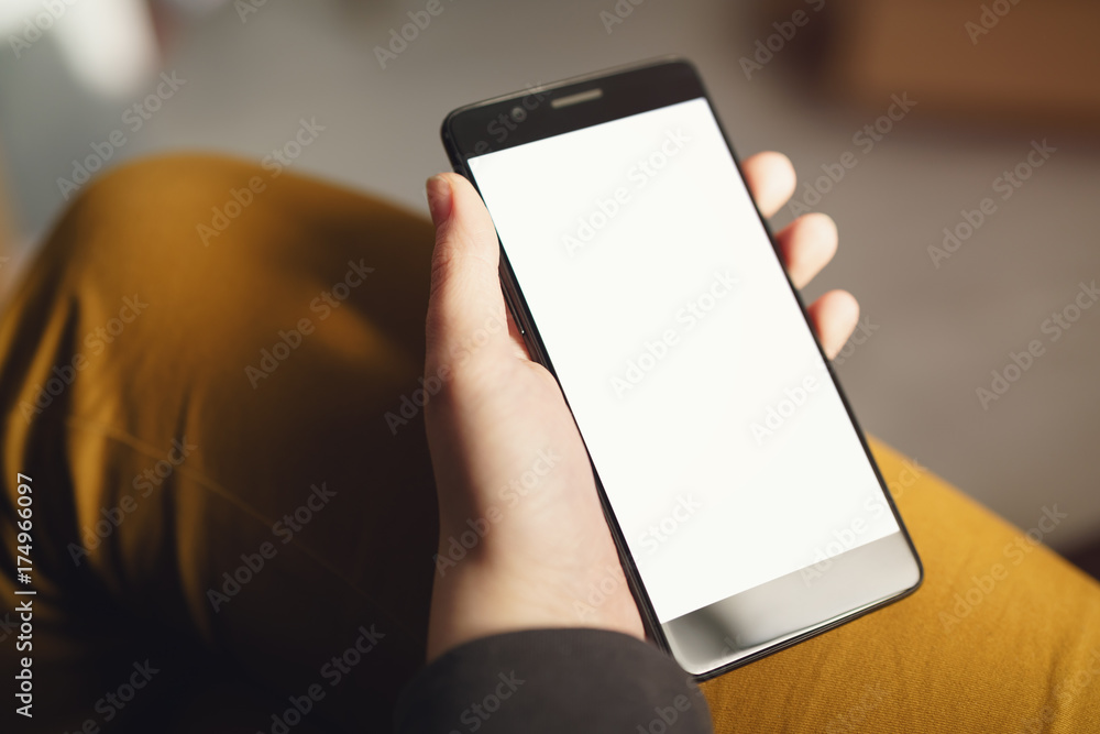 young female hands holding smartphone with white screen while sitting indoors young female hands holding smartphone with white screen while sitting indoors
