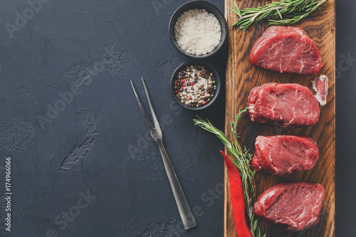 Filet mignon steaks and spices on wood at black background
