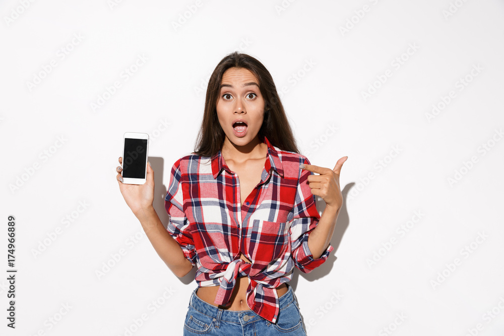 Amazed young pretty girl in checkered shirt showing thumb up gesture and holding smartphone Amazed young pretty girl in checkered shirt showing thumb up gesture and holding smartphone