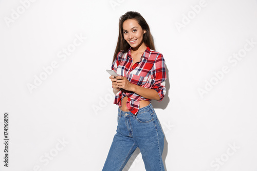 Photo of happy young woman wearing checkered shirt and blue jeans, chatting by phone