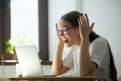 Young adult woman receiving good news via her laptop computer  reading email  videochatting with friends or watching a movie on online tv.