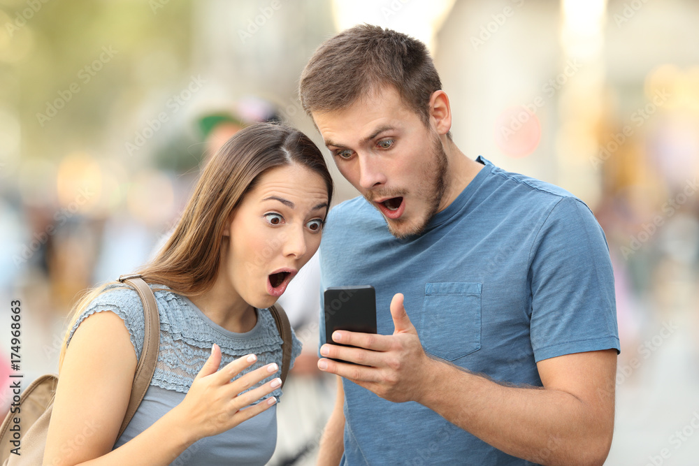 Amazed couple watching on line media in a phone Amazed couple watching on line media in a phone