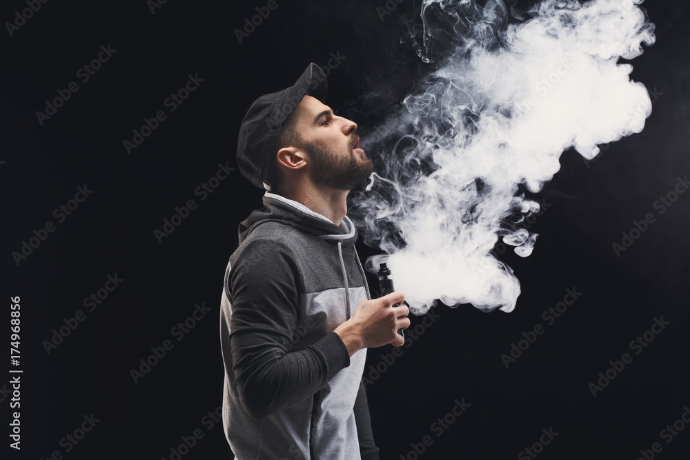 Young man vaping e-cigarette with smoke on black Young man vaping e-cigarette with smoke on black