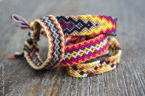 Four simple handmade homemade natural woven bracelets of friendship on wooden background, rainbow colors, checkered pattern