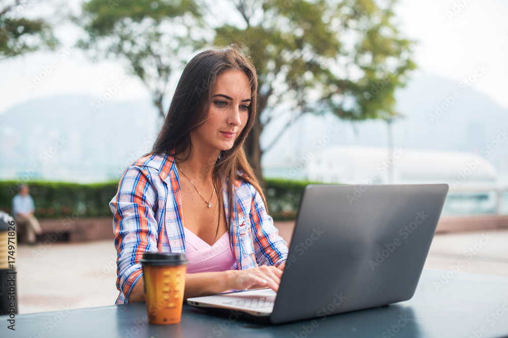 Young woman typing on a laptop studying or working in the park Young woman typing on a laptop studying or working in the park