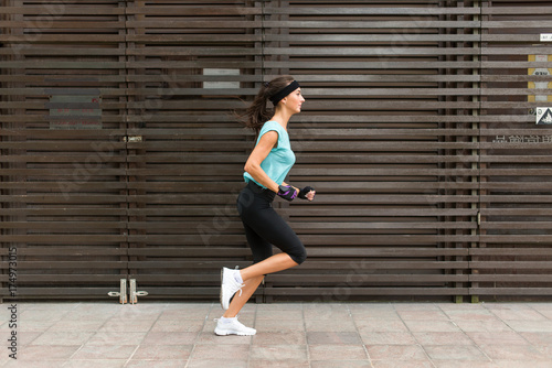 Side view of sporty young woman running on a sidewalk.