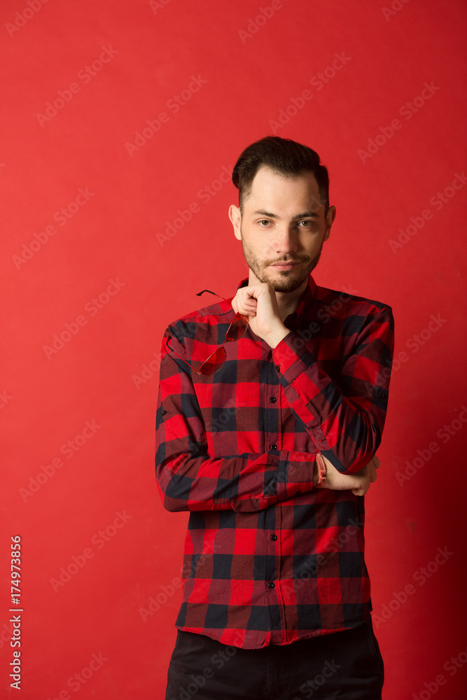 portrait of a stylish young guy in a plaid shirt on a red background