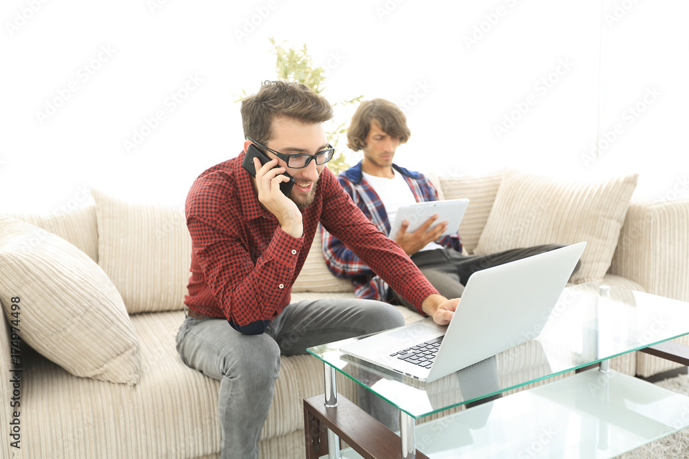 guy working on laptop and talking on smartphone sitting on couch guy working on laptop and talking on smartphone sitting on couch