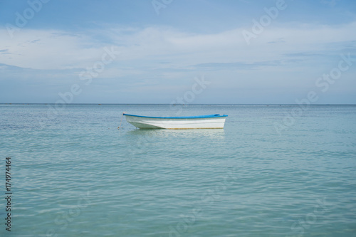 Small single fishing boat floating on the calm sea over blue sky background © stryjek