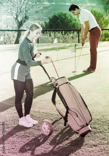 Female examining clubs while male hitting ball