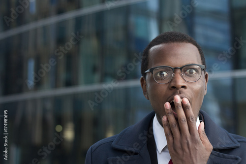 Foto Astonished bug-eyed dark-skinned businessman wearing suit, covering his mouth with one hand, looking shocked