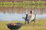 Man is sitting on a shore of river and making barbecue