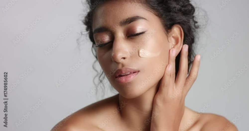 Young woman with beautiful olive skin applying liquid foundation or BB cream to her cheeks isolated on white Young woman with beautiful olive skin applying liquid foundation or BB cream to her cheeks isolated on white