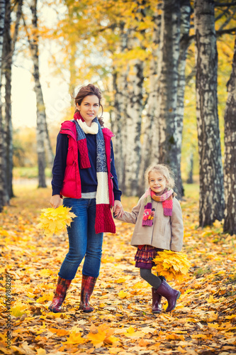 Smiling little girl and her mother enjoy walk in autumn park and play with bright autumn leaves