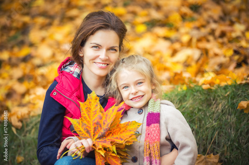 Smiling little girl and her mother enjoy walk in autumn park and play with bright autumn leaves