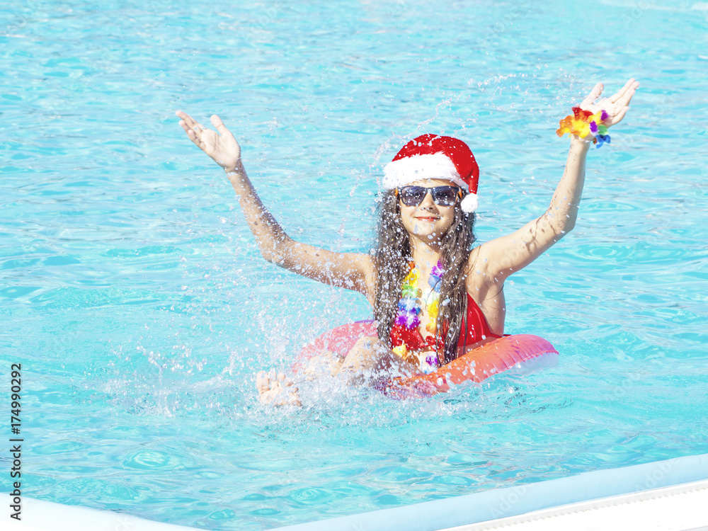 Beautiful young woman in Santa's hat with inflatable donut in swimming pool