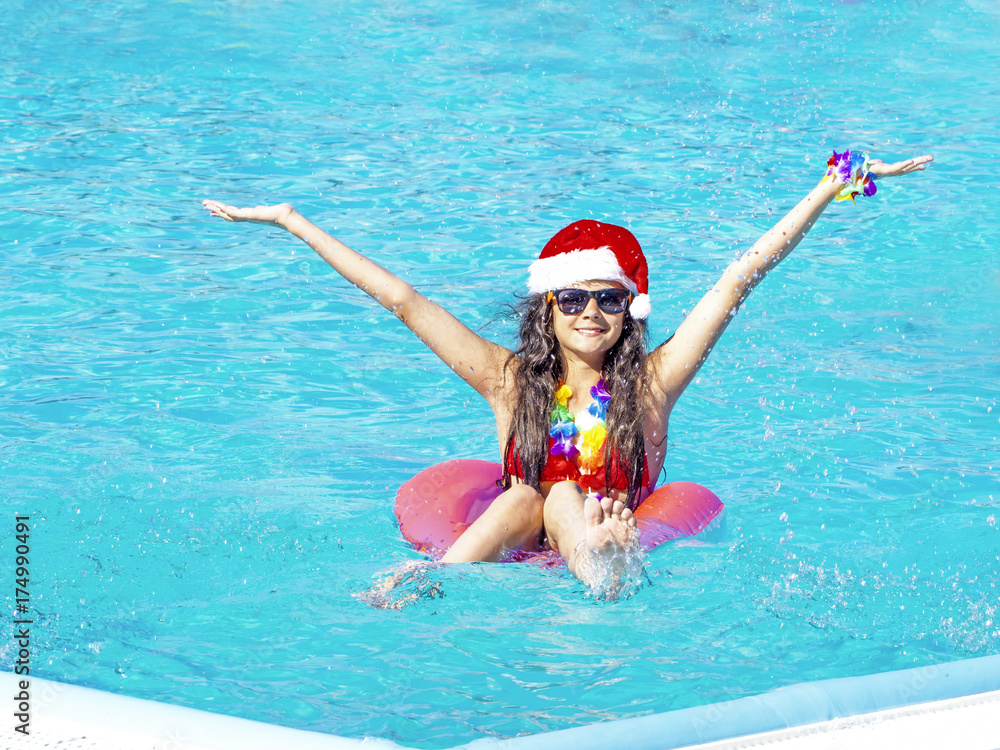 Beautiful young woman in Santa's hat with inflatable donut in swimming pool